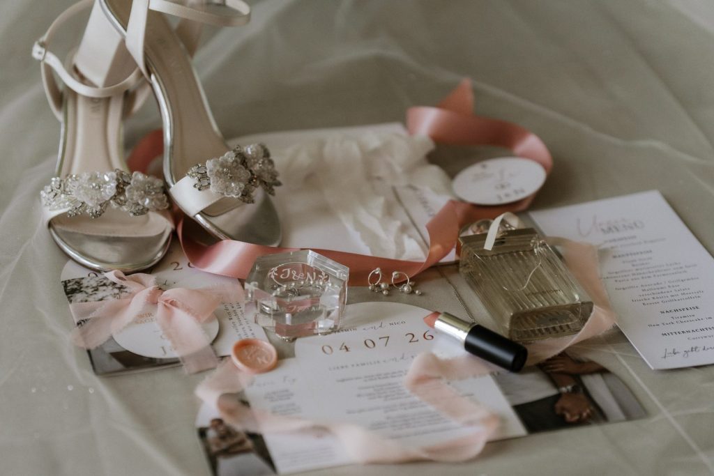 Flatlay mit Einladung, Ringen und Schleifen in Rosa- und Cremetönen